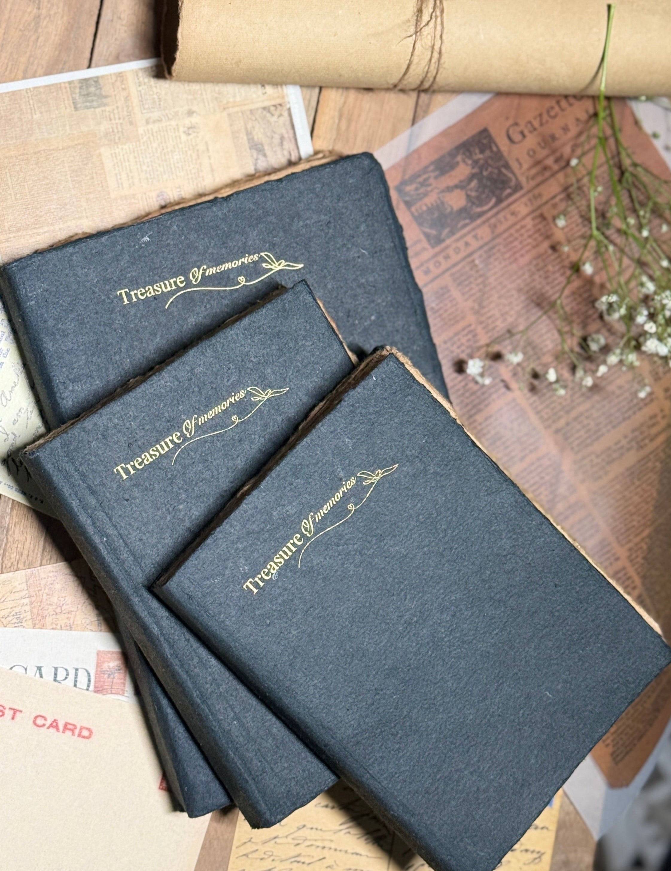 Three black cover books with gold embossed text on a wooden surface with vintage papers.